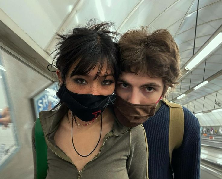 two people wearing masks on an escalator in a subway station, one with his head wrapped around the other's neck