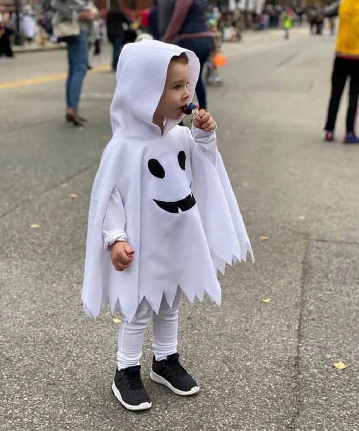 a little boy dressed up as a ghost on the street with people in the background