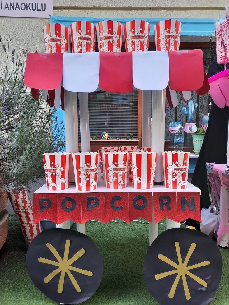 an outdoor popcorn stand with red and white paper cups on the top, in front of a window