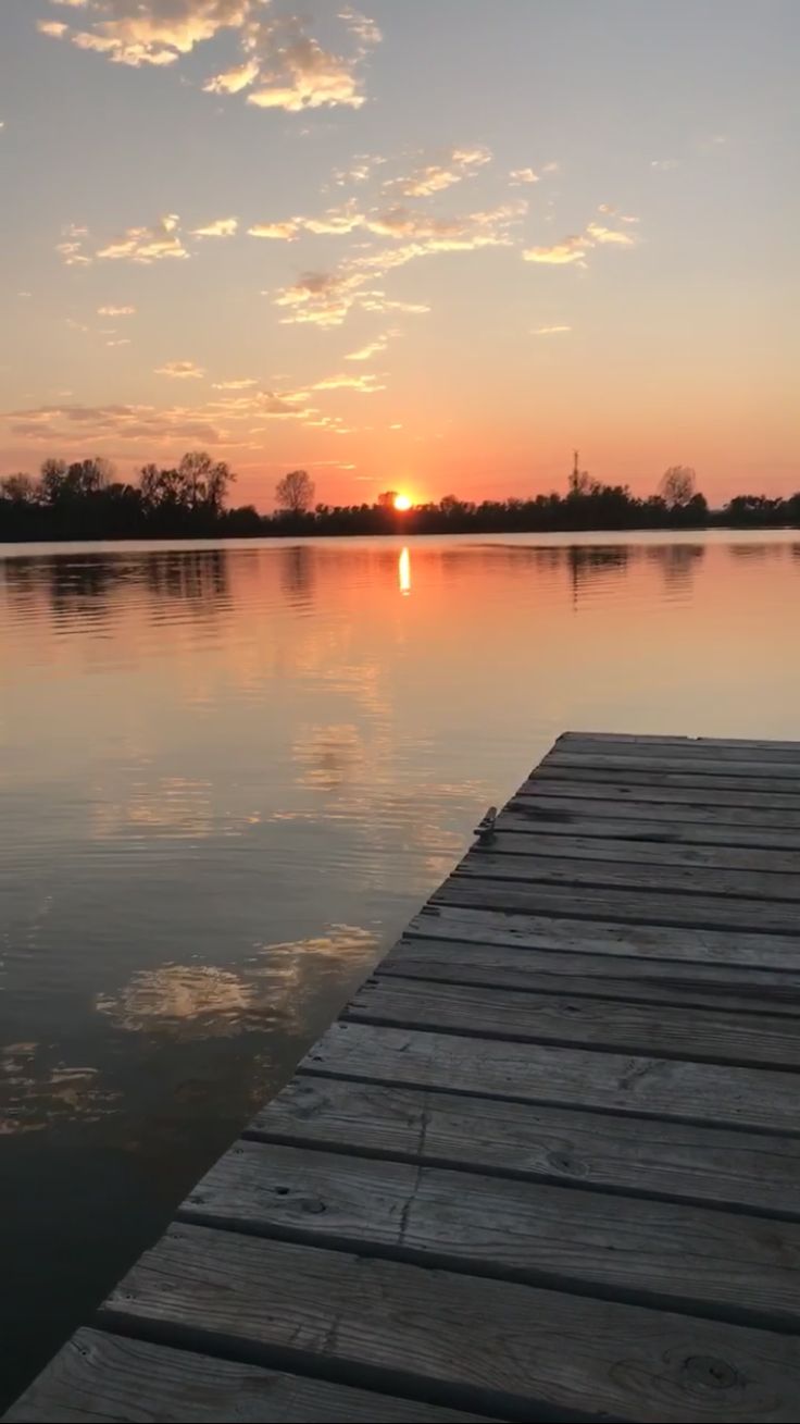 the sun is setting over water with a dock