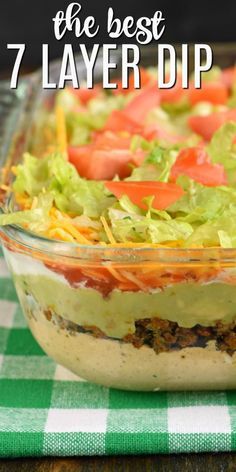 the best 7 layer dip recipe in a glass dish on a green and white checkered tablecloth