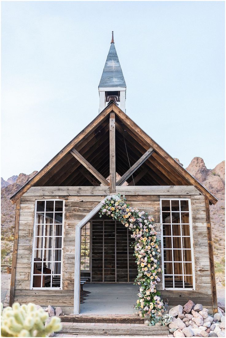 a bride and groom standing in front of an old wooden church with a floral arch