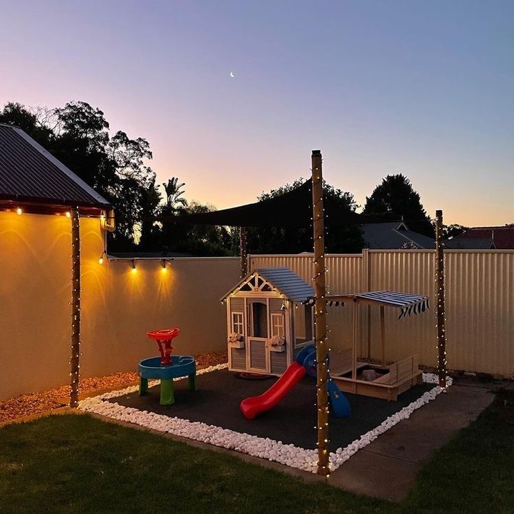 an outdoor play area is lit up at night with lights on the fence and in the back ground