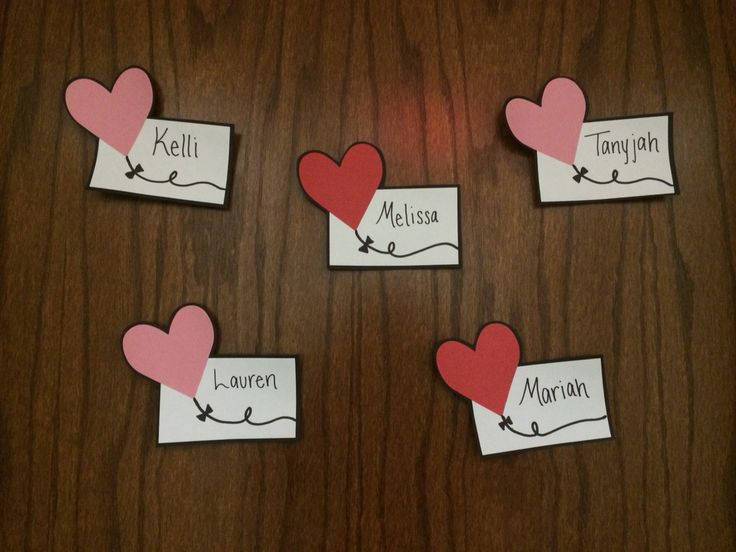 four pieces of paper with hearts and name tags attached to them on a wooden surface