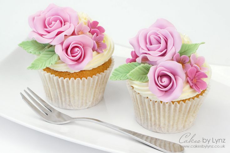 two cupcakes decorated with pink flowers and green leaves on a plate next to a fork