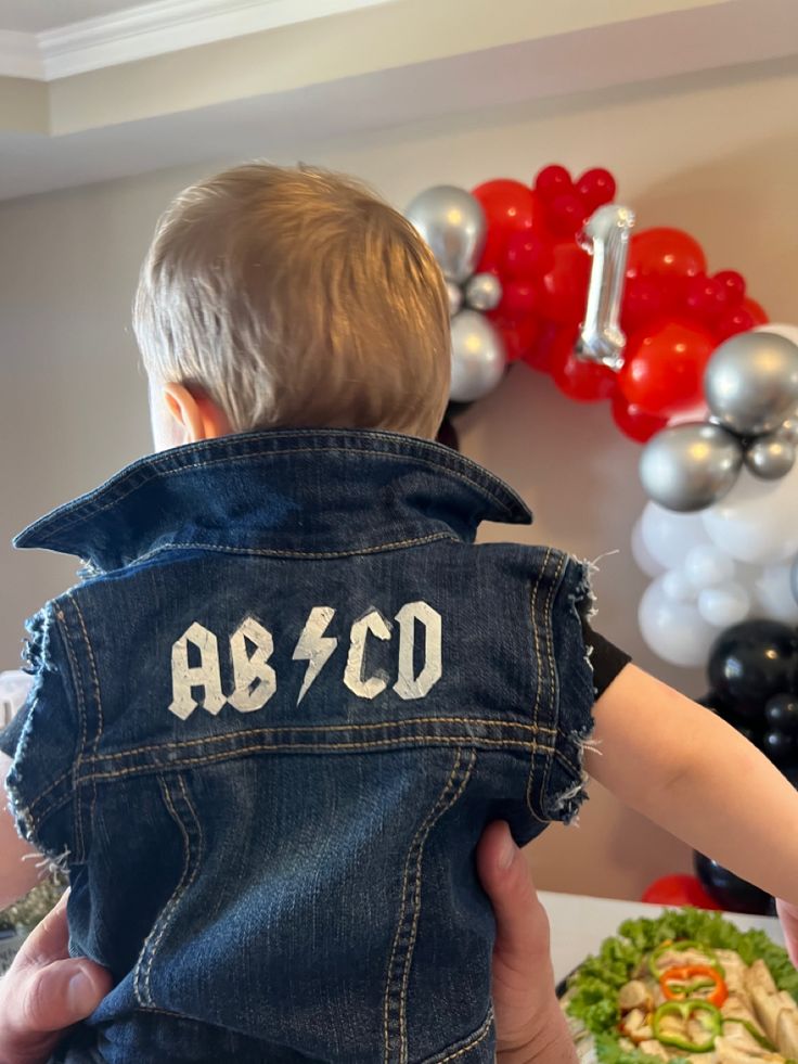 a man holding a small child in his lap while wearing a jean jacket with the word ab co on it