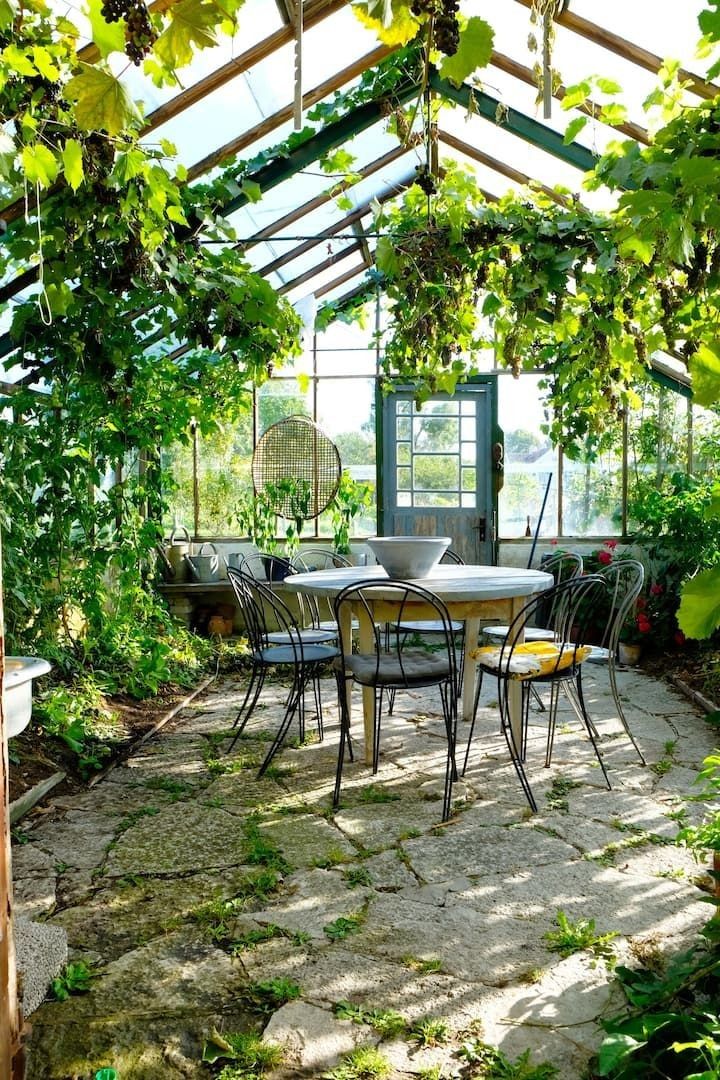 an outdoor table and chairs under a green roof in a garden with lots of greenery