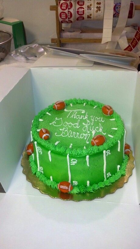 a green birthday cake with footballs on it in a white box, ready to be eaten