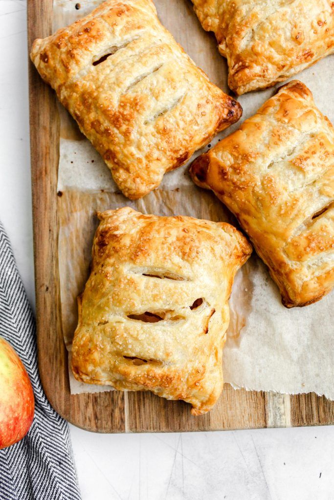 four apple turnovers sitting on top of a wooden cutting board next to an apple