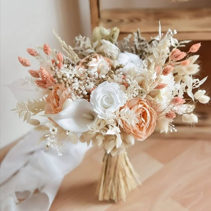 a bridal bouquet with peach and white flowers on a wooden table in front of a mirror