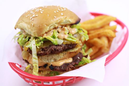 a hamburger with lettuce, cheese and onions in a red basket next to french fries