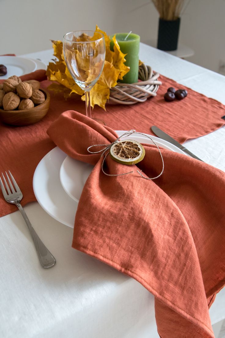 the table is set with an orange linen napkin and silverware, along with some fruit and nuts