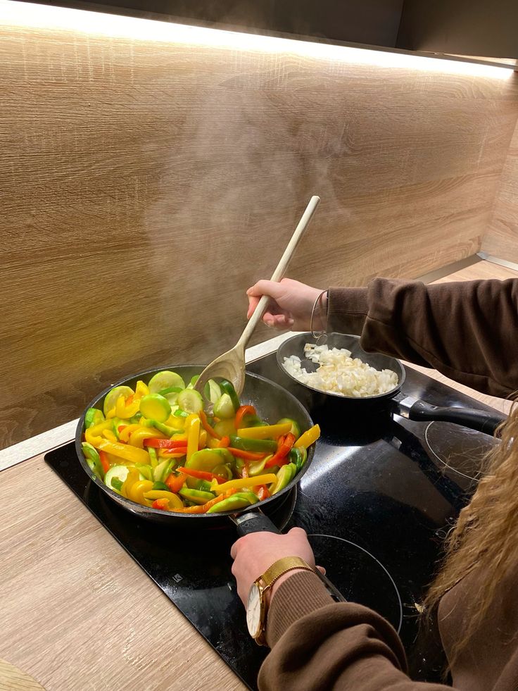 a woman stirs vegetables in a wok on the stove