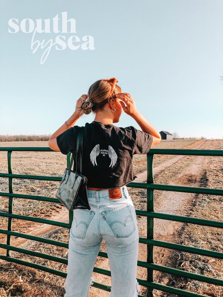 a woman standing in front of a fence looking at the sky with her hand on her head