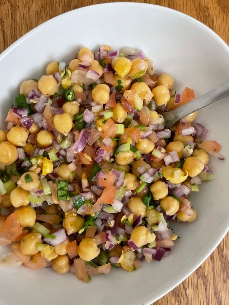 a white bowl filled with chickpeas, onions and cilantro on top of a wooden table