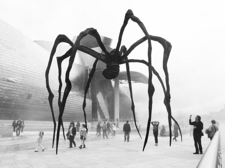 a giant spider sculpture in front of a building with people standing around it and looking at it