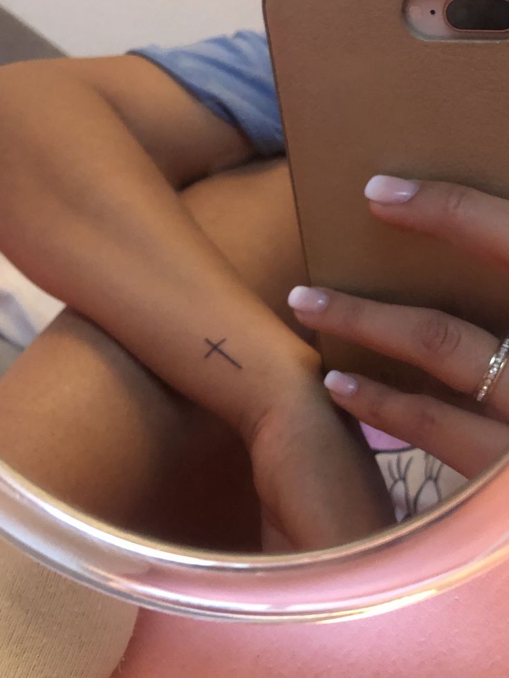 a woman's hand with a small cross tattoo on her left wrist, in front of a mirror