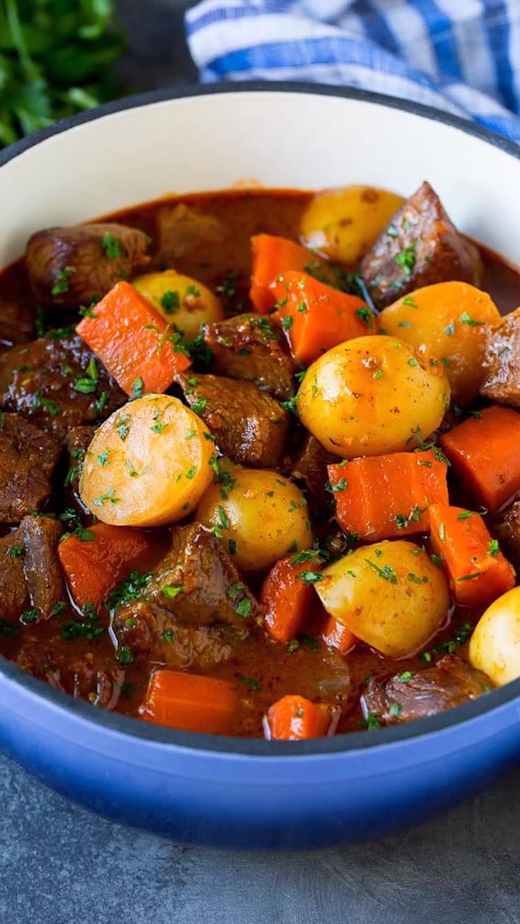 a blue bowl filled with stew and potatoes on top of a gray table next to some parsley