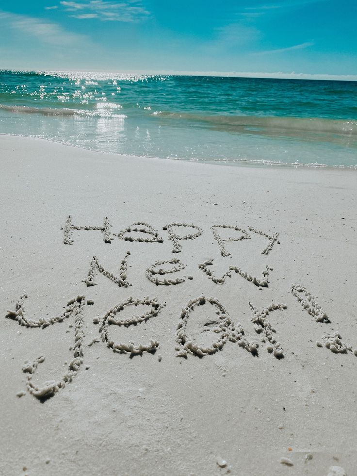 happy new year written in the sand at the beach