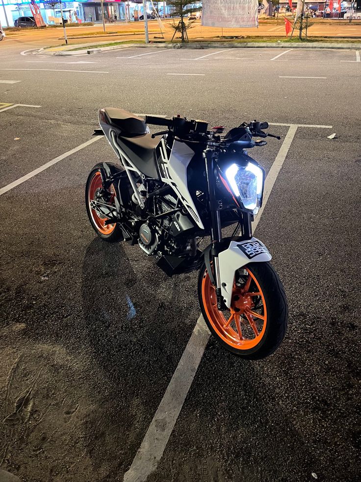 an orange and white motorcycle is parked in a parking lot with no one around it