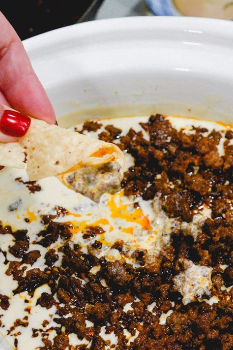 a hand dipping a tortilla chip into a bowl filled with ground beef and cheese