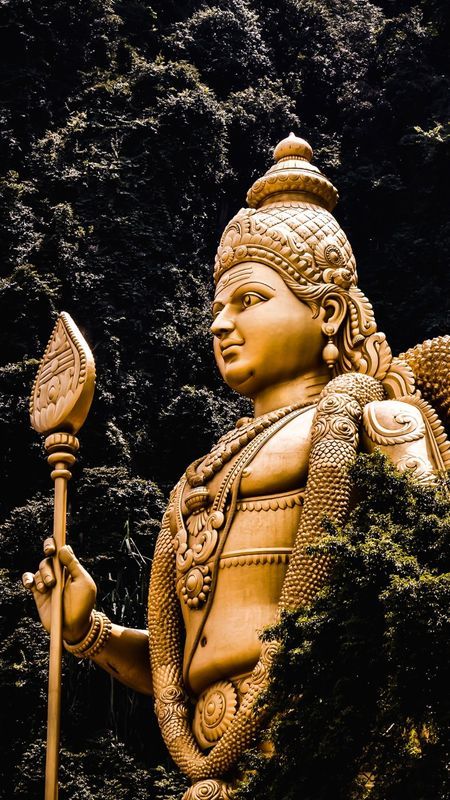 a statue of a person holding a spear and wearing a helmet with trees in the background