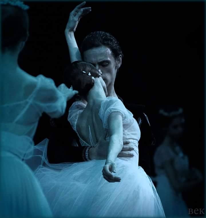 a woman in a white dress is dancing with another woman wearing a blue dress behind her