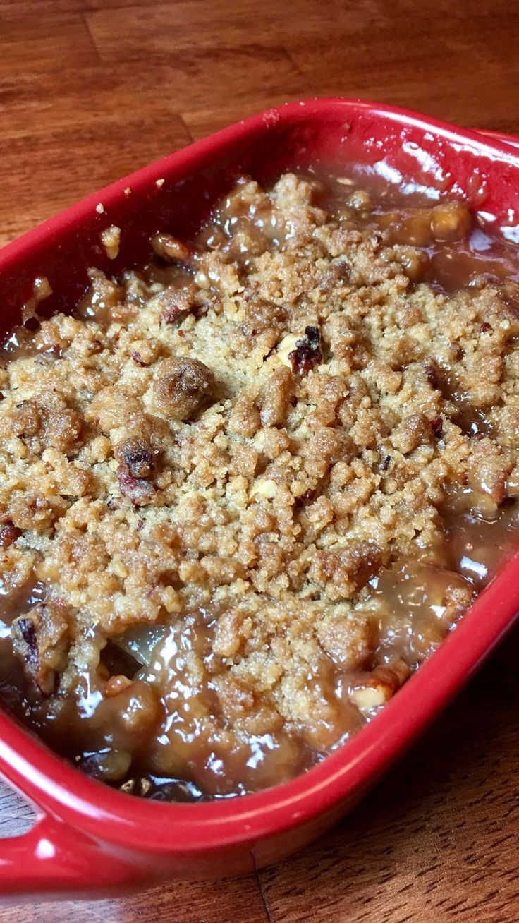 a red casserole dish filled with fruit and crumbled toppings on top of a wooden table