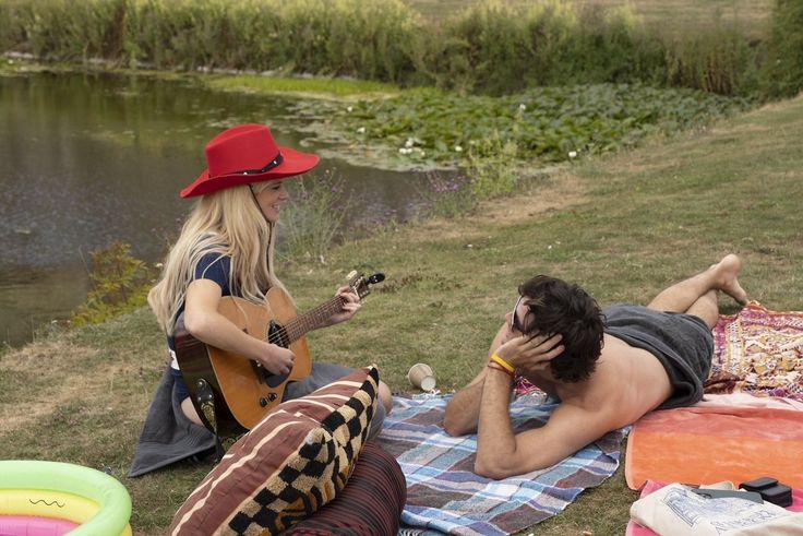 two people are sitting on the grass playing guitar and singing to someone else with a red hat