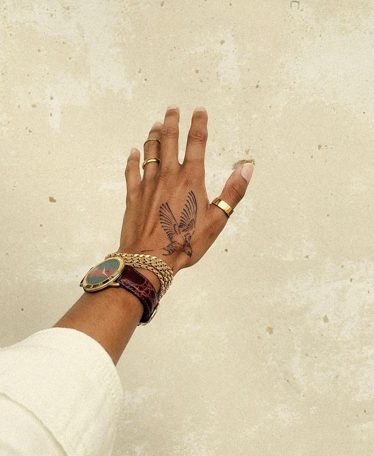 a woman's hand with a bird tattoo on her left wrist and gold bracelet