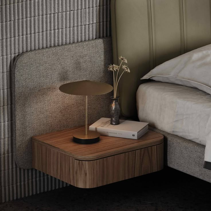 a bedside table with a book on it next to a lamp and bed headboard