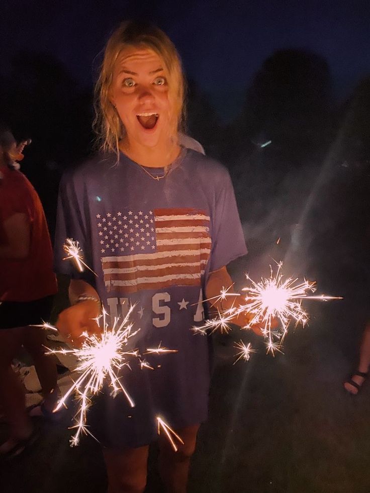 a woman holding sparklers in her hands with an american flag t - shirt on