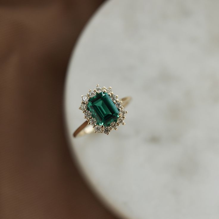 an emerald and diamond ring sitting on top of a table