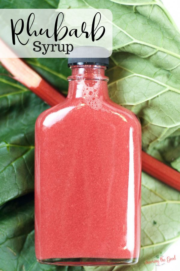 a bottle filled with red liquid sitting on top of a green leafy plant next to a