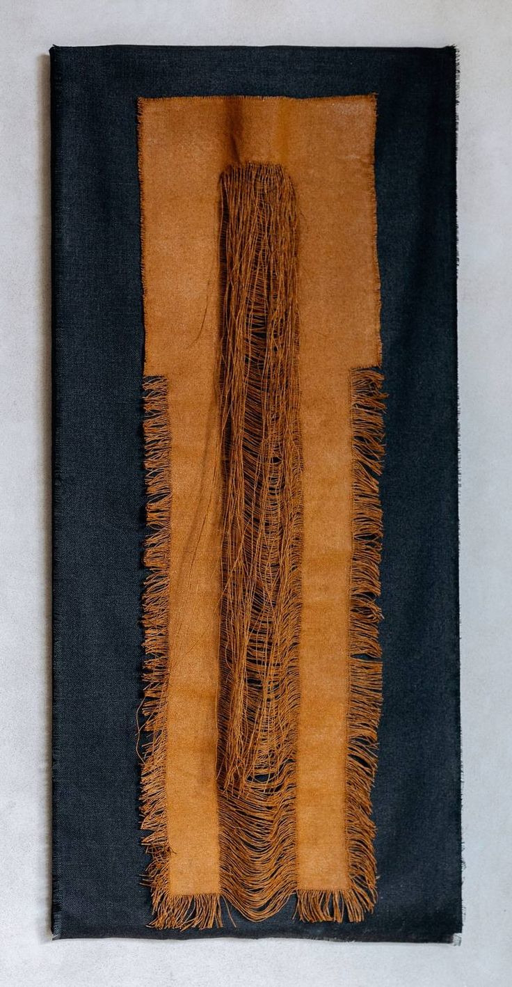 an orange and black piece of cloth with fringes on the edges, hanging on a wall