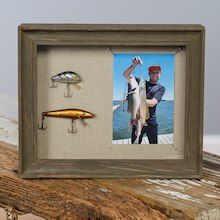 a man holding a fish and fishing lures in front of a picture frame on a piece of wood