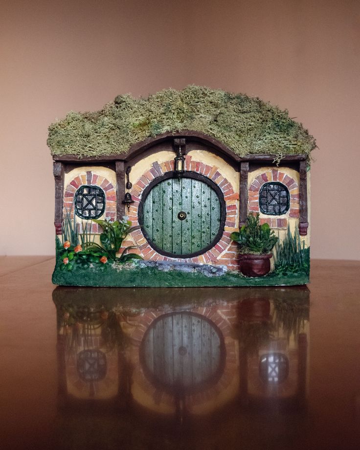 a small house made out of clay with a green door and plants on the outside