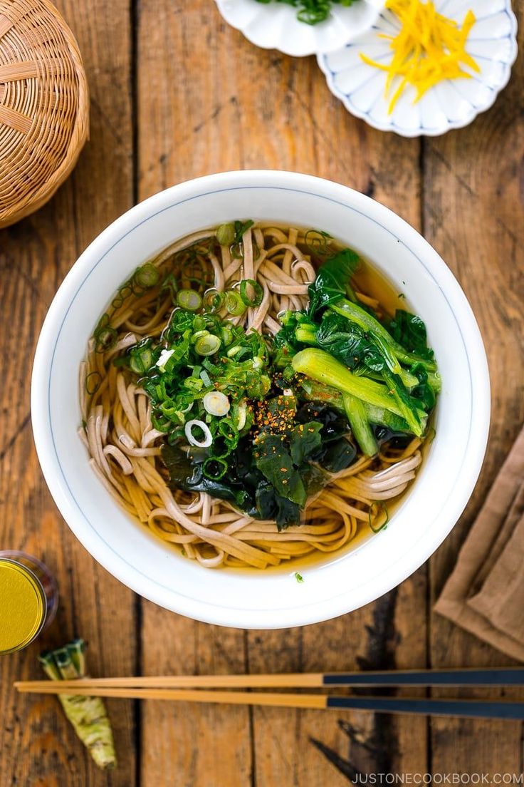 a white bowl filled with noodles and broccoli on top of a wooden table