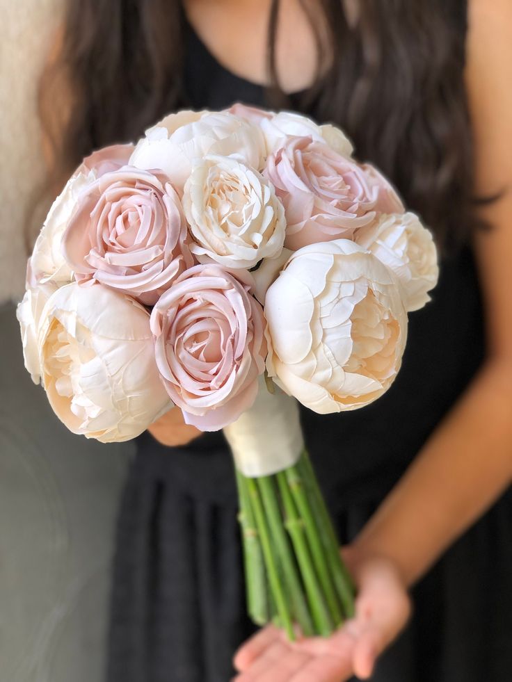 a woman in a black dress holding a bouquet of white and pink flowers with her hands