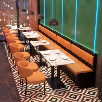 an empty restaurant with orange chairs and green screen behind the booth area, along with white tablecloths and place settings