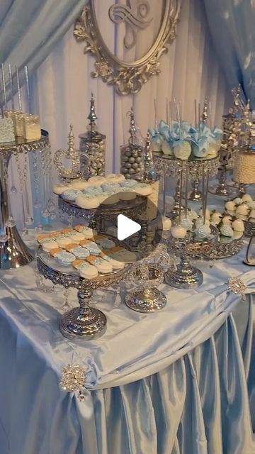 a table topped with lots of cakes and cupcakes next to a wall covered in blue drapes