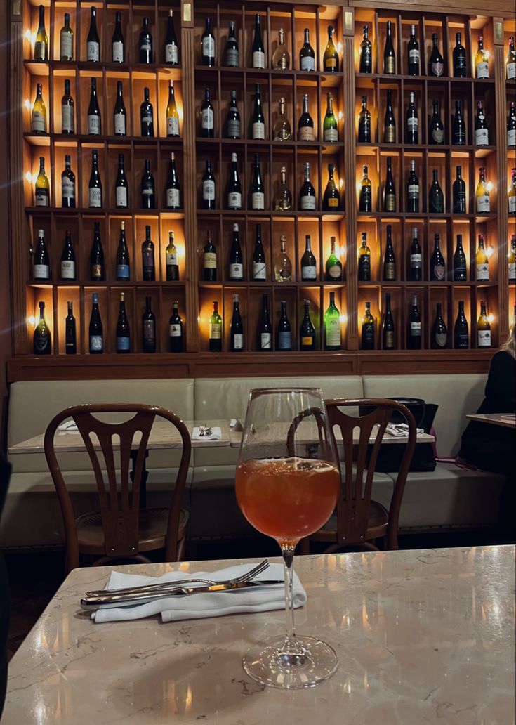 a wine glass sitting on top of a table next to a wall filled with bottles