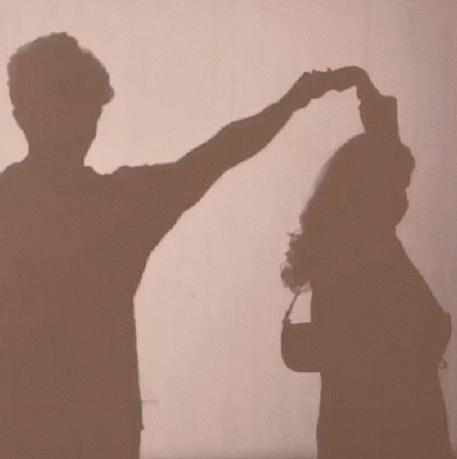 two people standing in front of a wall with the shadow of one person on it