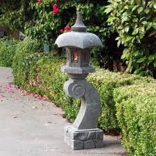 a stone lantern sitting on the side of a road next to bushes and trees with red flowers