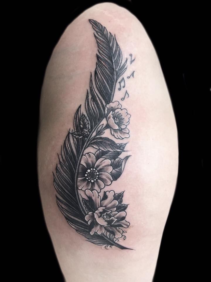 a woman's thigh with a feather and flowers tattoo on the side of her leg