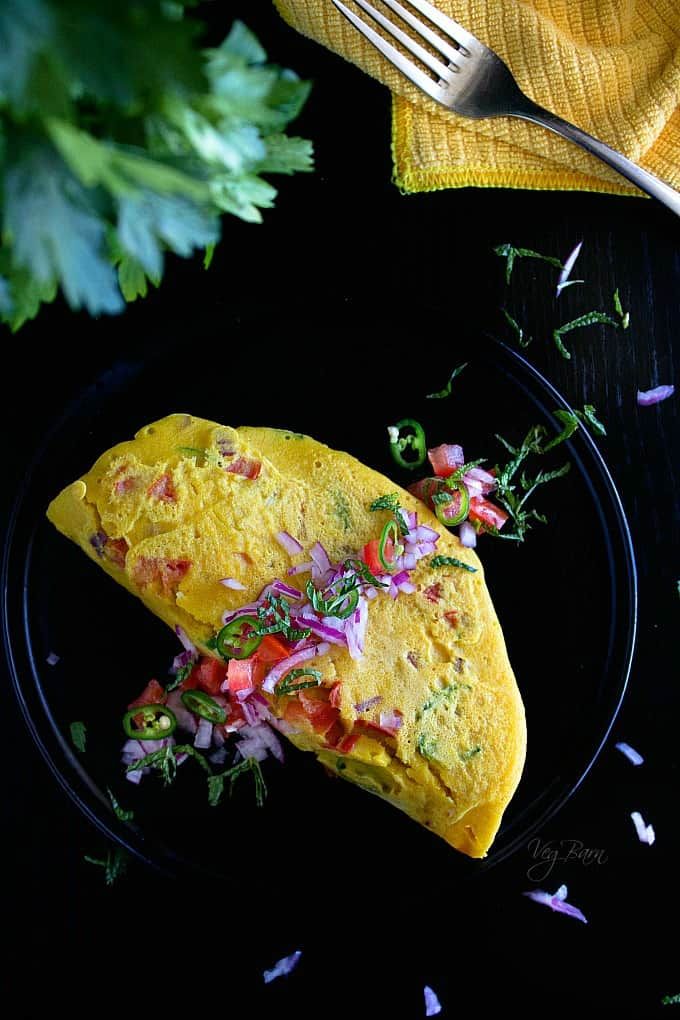 an omelet on a black plate next to a fork and some cilantro