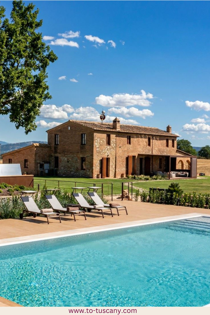 an outdoor swimming pool in front of a large brick house with lawn chairs around it