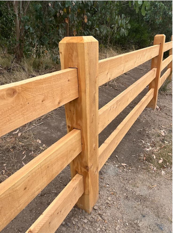 a wooden fence in the middle of a dirt area with trees and bushes behind it