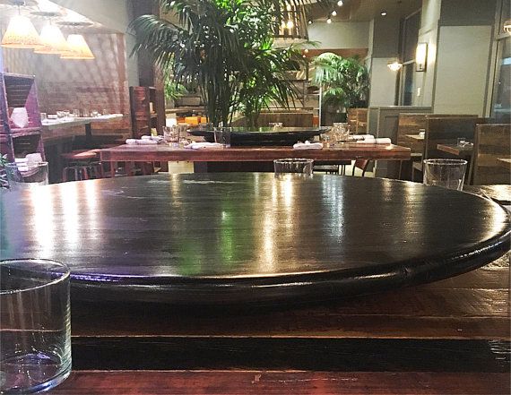 a large wooden table in a restaurant next to a tall potted plant and two glasses on the table