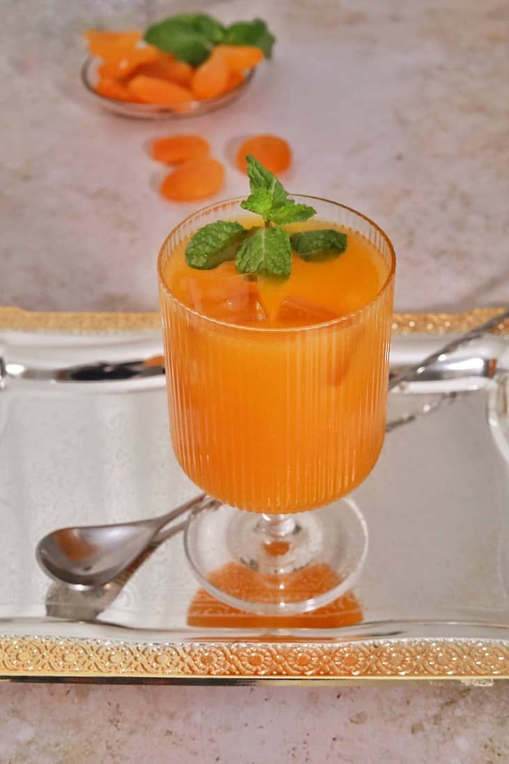 an orange drink with mint garnish in a glass on a silver tray